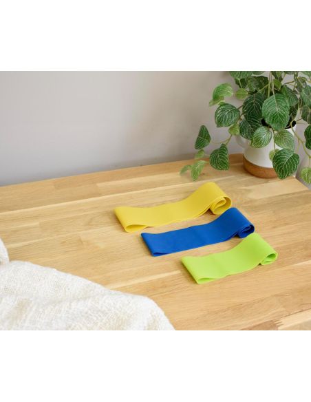 Set de 3 bandas elásticas de fitness personalizado, las 3 bandas sobre un suelo de madera junto a una planta