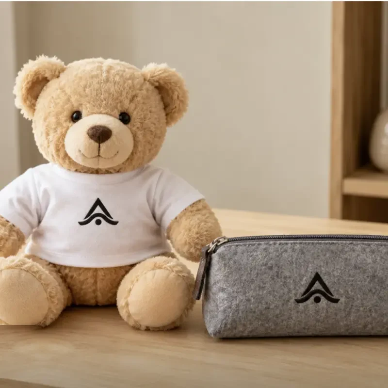 Peluche y estuche escolar personalizados con el mismo logo, sobre un escritorio de madera clara