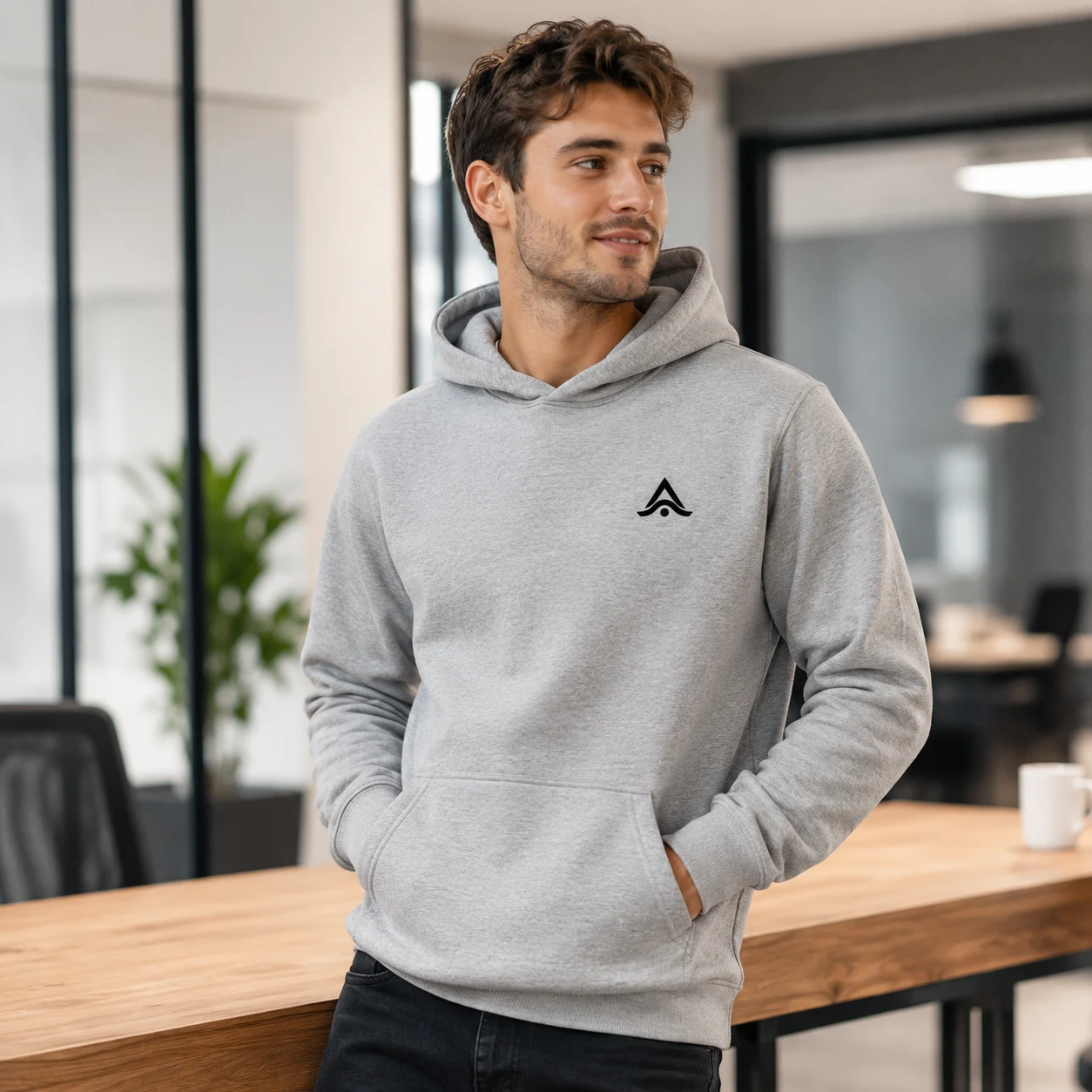 Chico con sudadera personalizada gris y logo bordado en el pecho en una oficina